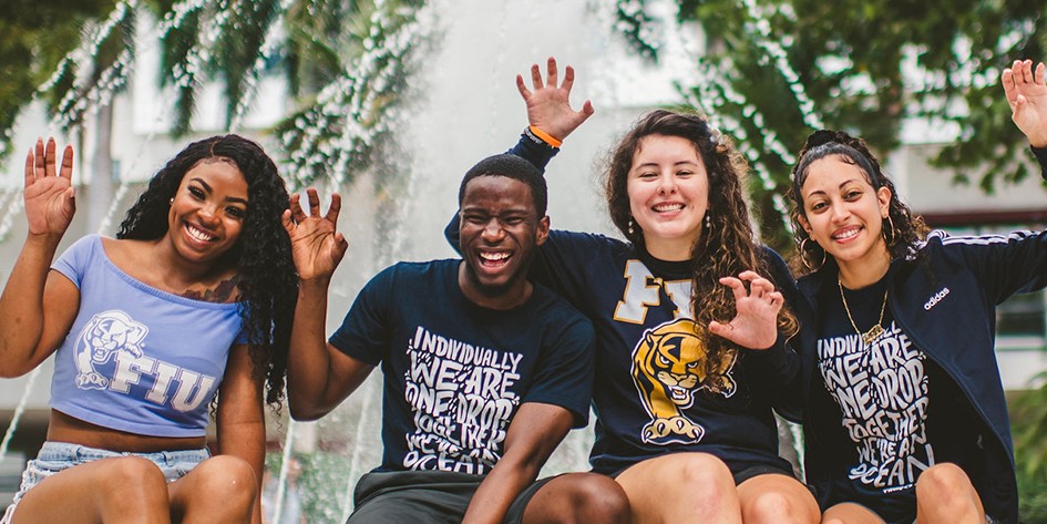 Group of students posing for a picture while smiling and waving at the camera.