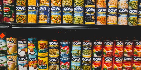 Grocery store shelf lined with cans of perishable food items. 